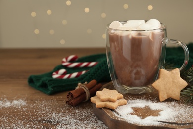 Hot drink with marshmallows, cookies and cinnamon on wooden table. Space for text