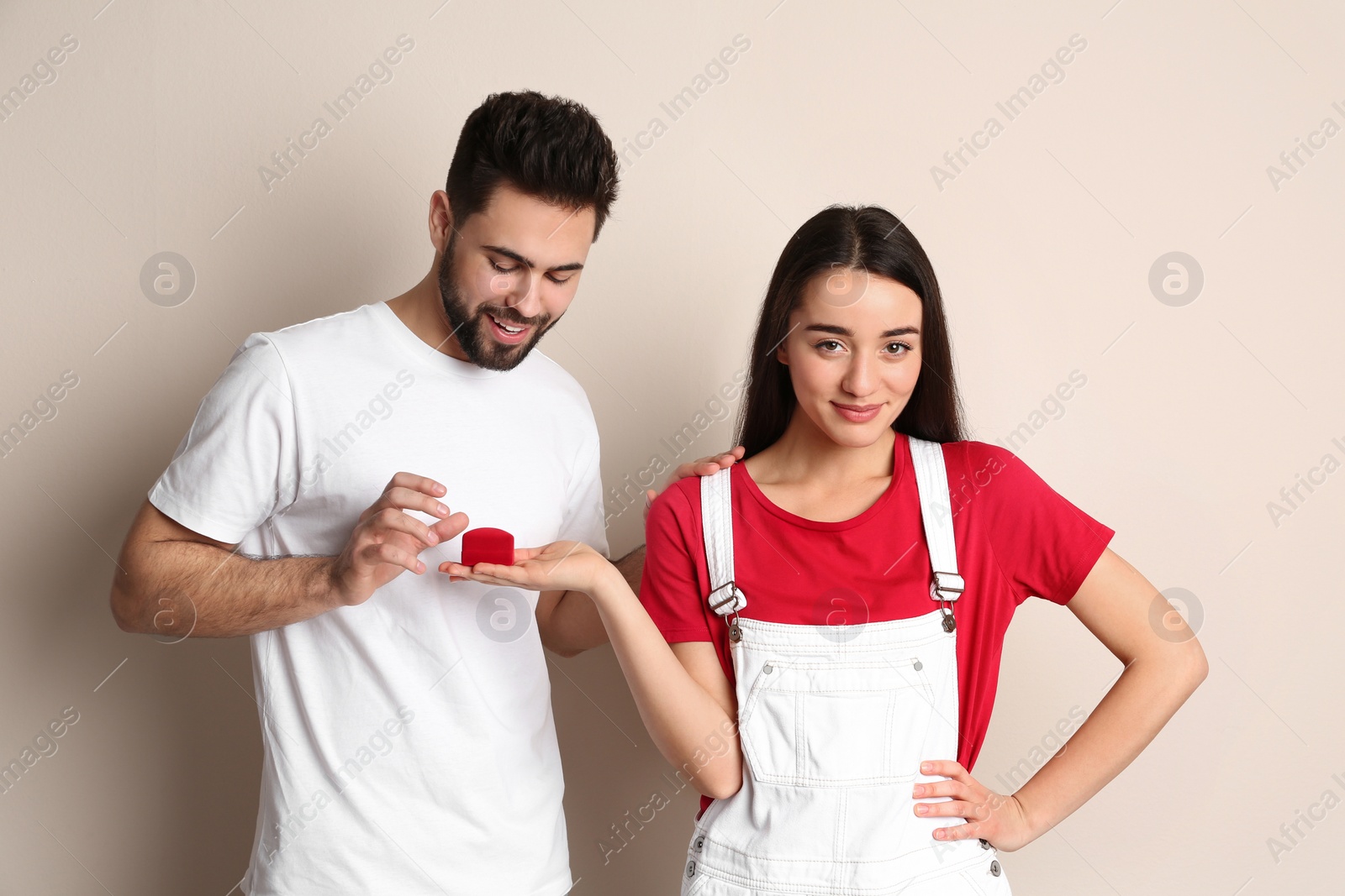 Photo of Young woman with engagement ring making marriage proposal to her boyfriend on beige background