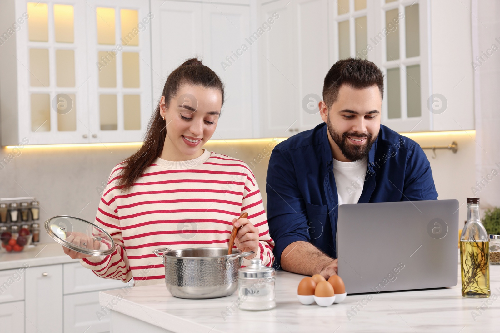 Photo of Happy lovely couple using laptop while cooking in kitchen