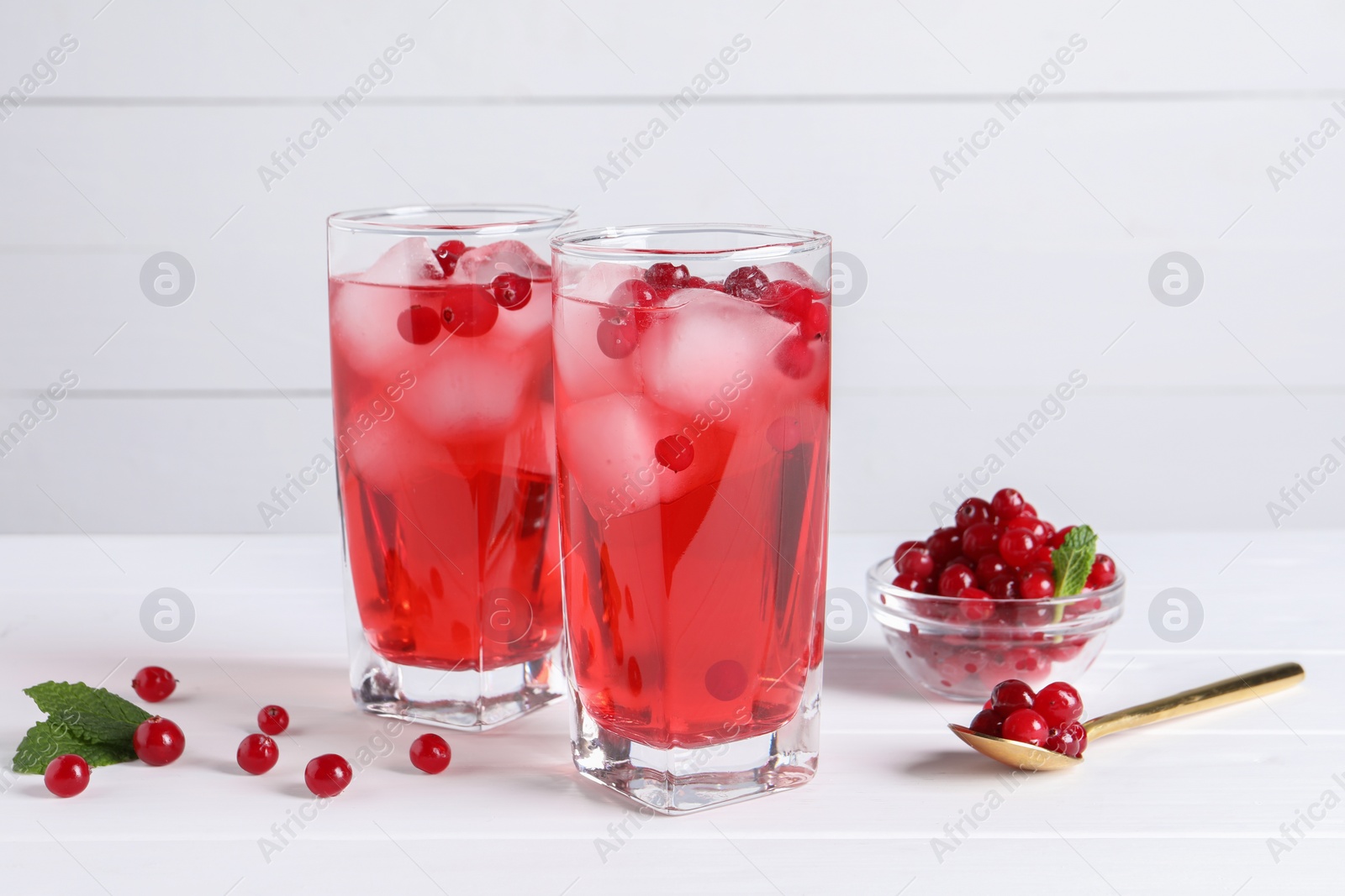 Photo of Tasty cranberry juice with ice cubes in glasses and fresh berries on white wooden table