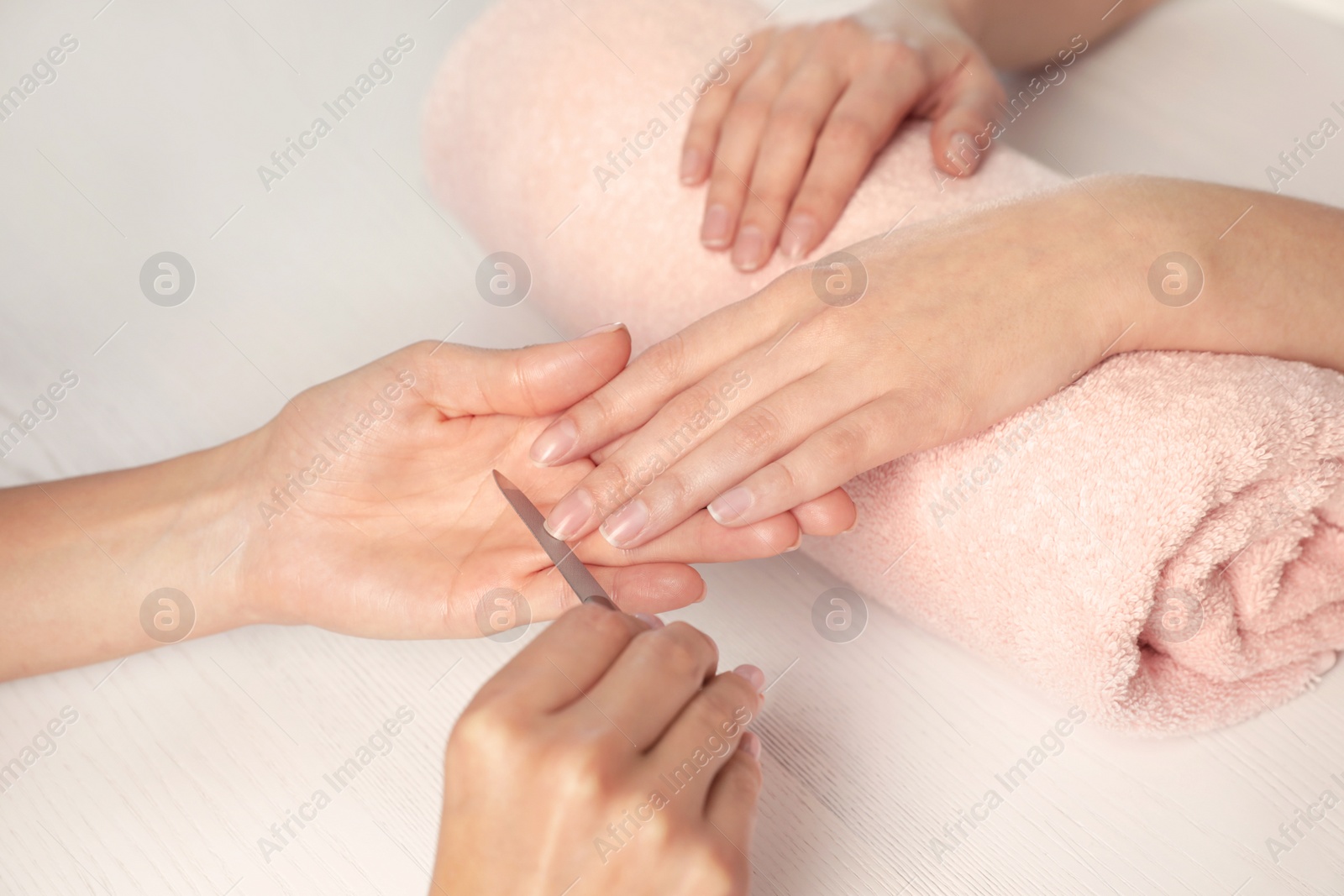 Photo of Manicurist filing client's nails at table, closeup. Spa treatment