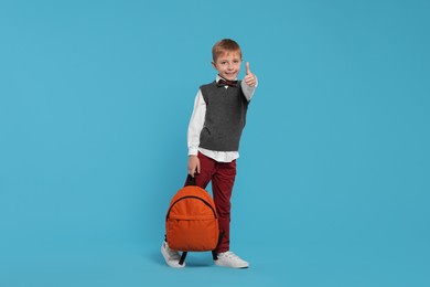 Photo of Happy schoolboy with backpack showing thumb up gesture on light blue background
