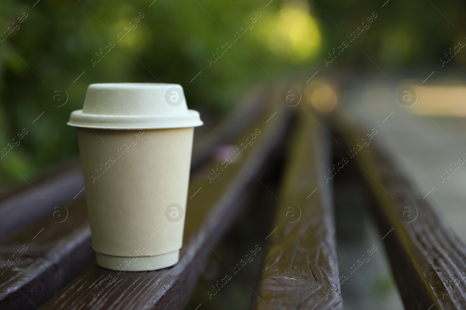 Photo of Cardboard takeaway coffee cup with lid on wooden bench outdoors, space for text