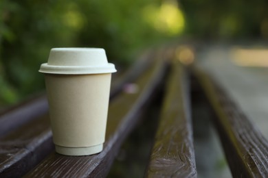 Photo of Cardboard takeaway coffee cup with lid on wooden bench outdoors, space for text