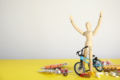 Photo of Pills, sportsman and bike model on yellow table, space for text. Using doping in cycling sport concept