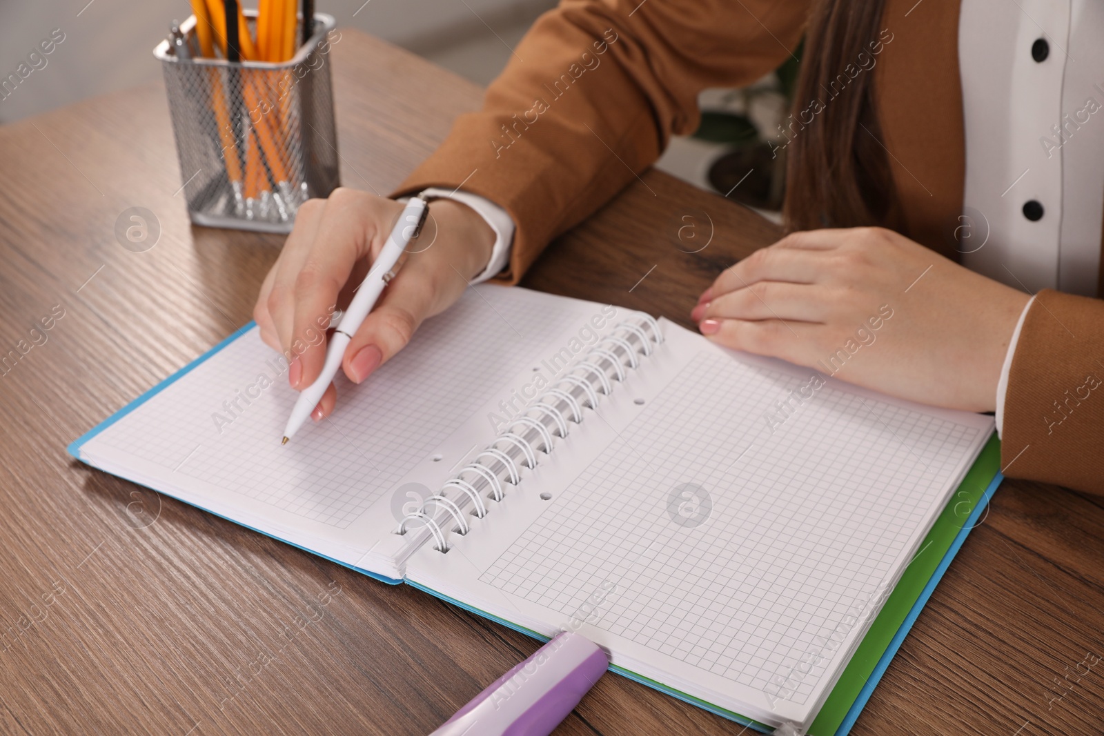 Photo of Woman taking notes at wooden table indoors, closeup