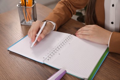 Woman taking notes at wooden table indoors, closeup