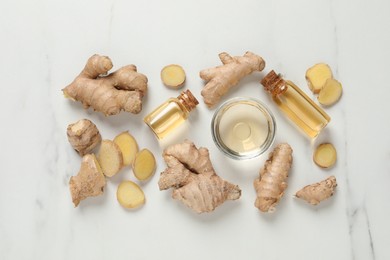 Glass bottles of essential oil and ginger root on white marble table, flat lay