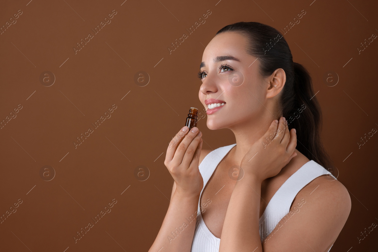 Photo of Beautiful happy woman with bottle of essential oil on brown background, space for text