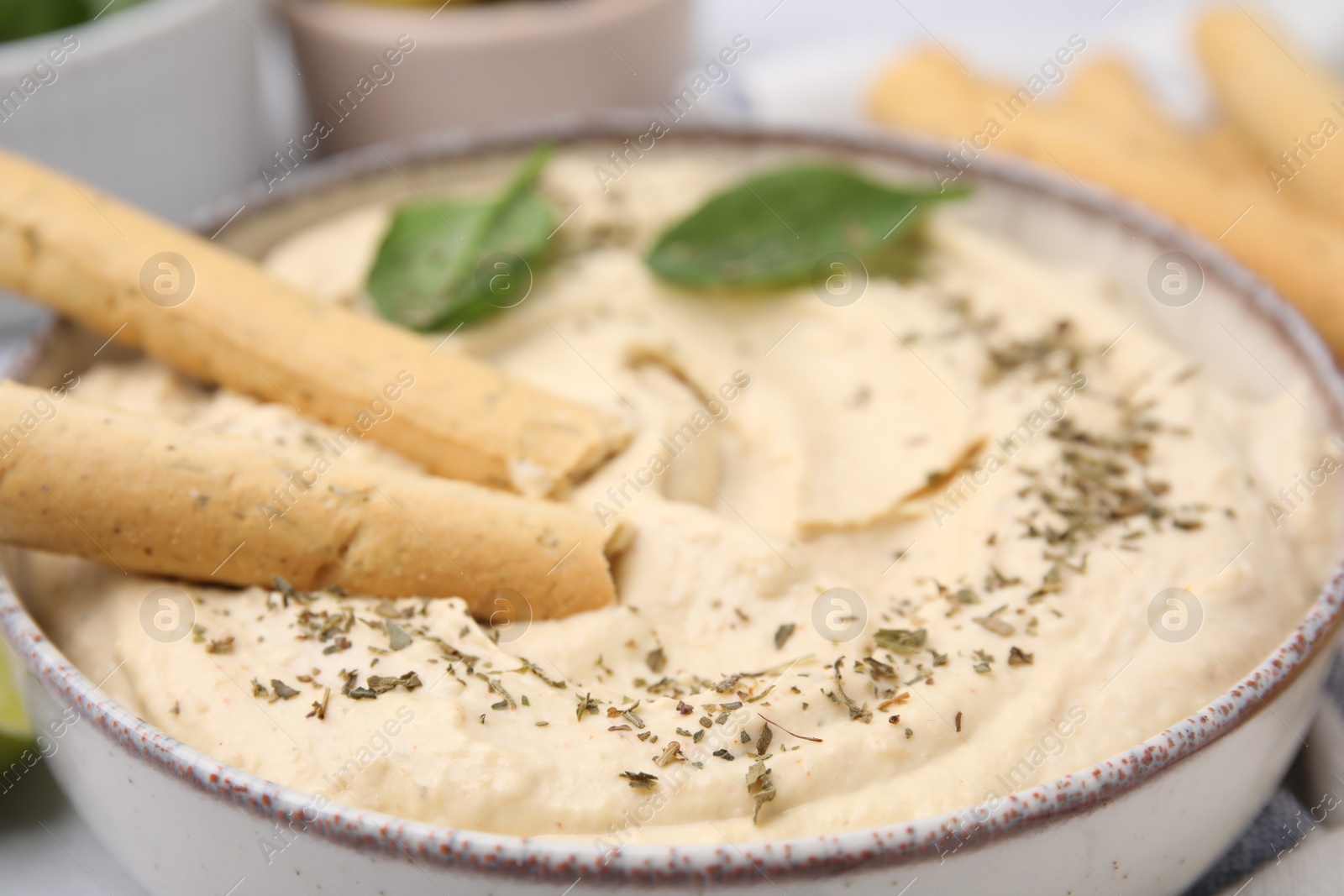 Photo of Delicious hummus with grissini sticks on table, closeup