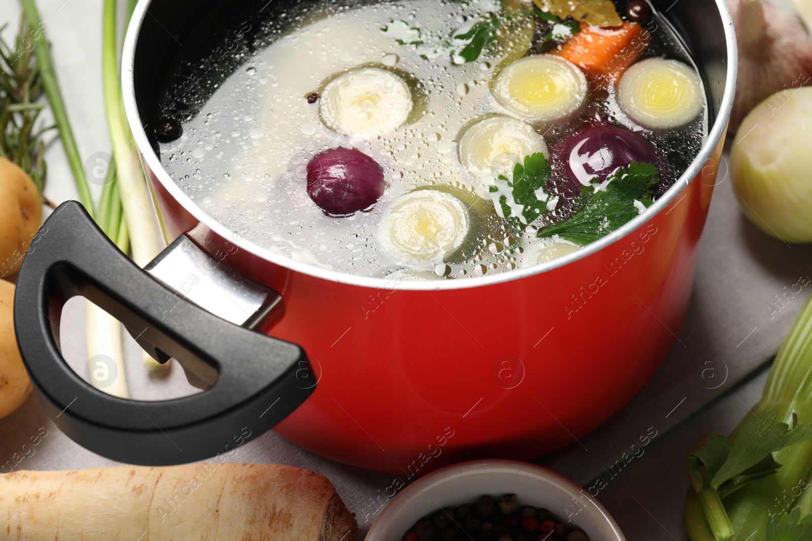 Photo of Pot with tasty bouillon and different ingredients on light grey table, closeup