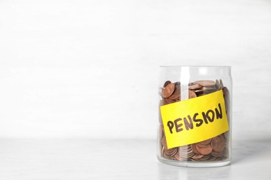 Coins in glass jar with label "PENSION" on table against light wall. Space for text