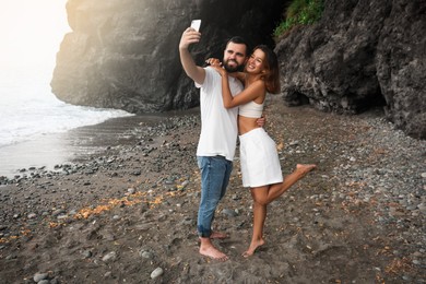 Photo of Happy young couple taking selfie on beach near sea. Space for text
