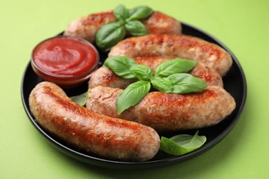 Photo of Plate with tasty homemade sausages, ketchup and basil leaves on green table, closeup