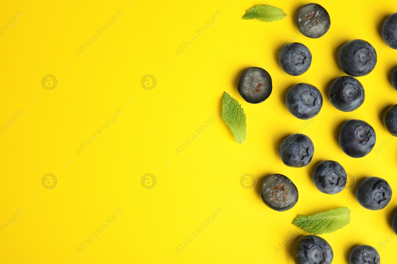 Photo of Tasty ripe blueberries and leaves on yellow background, flat lay with space for text