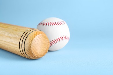 Photo of Wooden baseball bat and ball on light grey background, space for text. Sports equipment