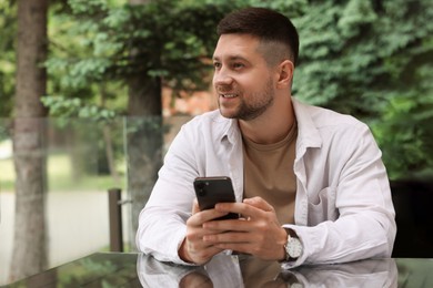 Photo of Handsome man sending message via smartphone at table in outdoor cafe