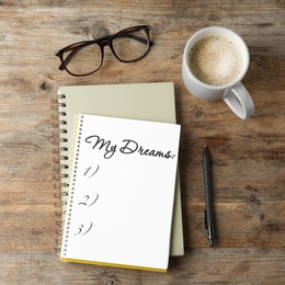 Image of Notebook with dreams list on wooden table, flat lay 
