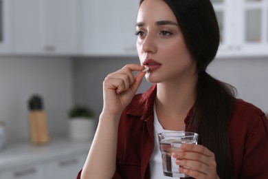 Photo of Depressed woman with glass of water taking antidepressant pill indoors, space for text