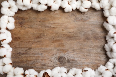 Frame of cotton flowers on wooden background, flat lay. Space for text