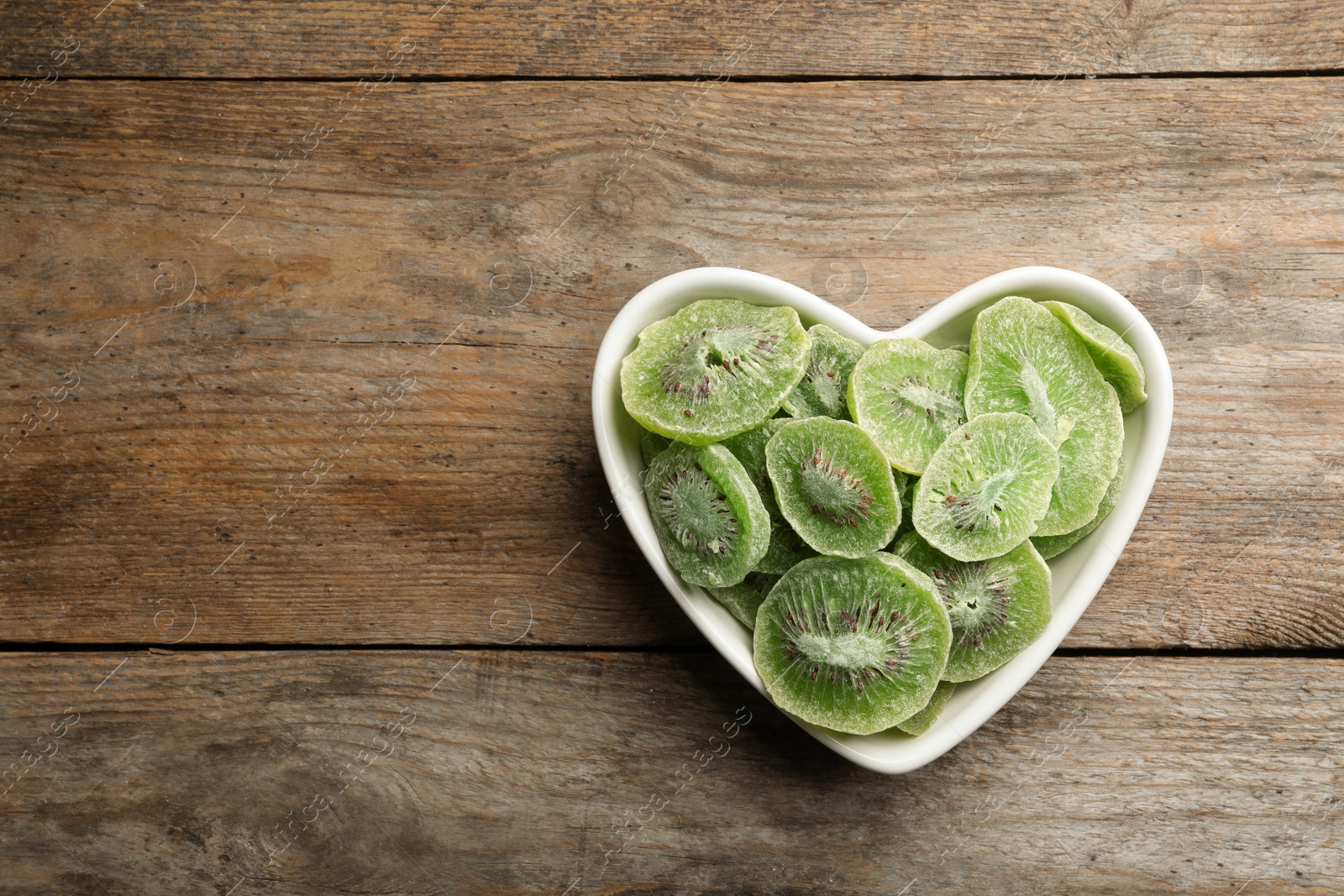 Photo of Bowl of dried kiwi on wooden background, top view with space for text. Tasty and healthy fruit