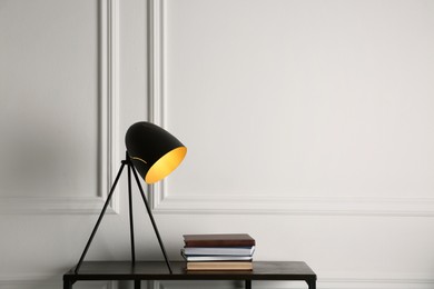 Photo of Wooden table with books and modern lamp near white wall, space for text. Interior element