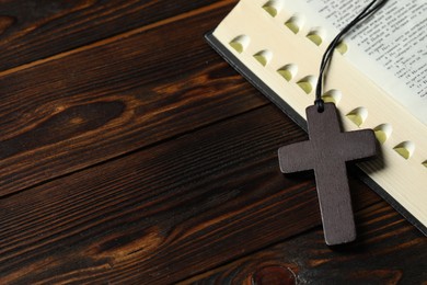 Wooden Christian cross and Bible on table, closeup. Space for text