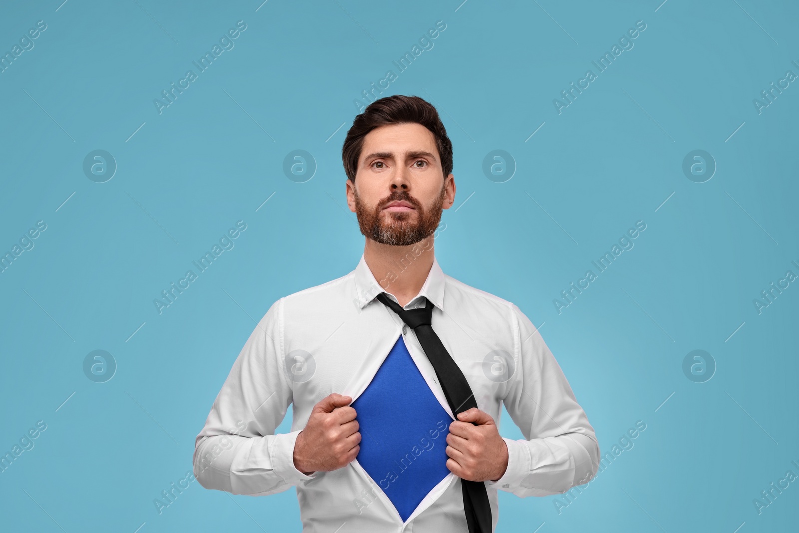 Photo of Confident businessman wearing superhero costume under suit on light blue background