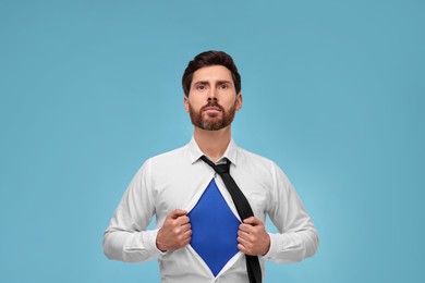 Confident businessman wearing superhero costume under suit on light blue background