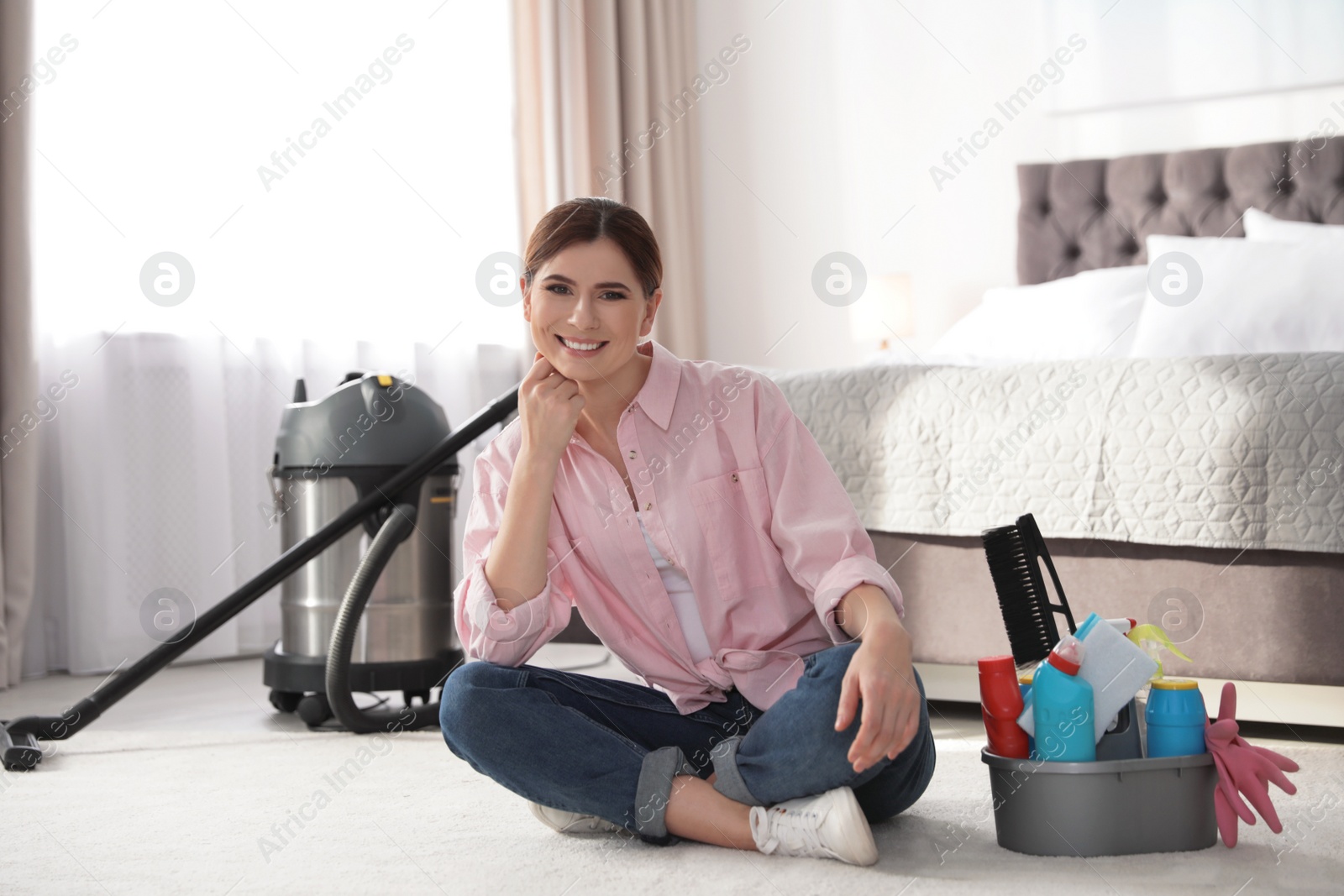 Photo of Happy woman with cleaning products sitting on floor in bedroom