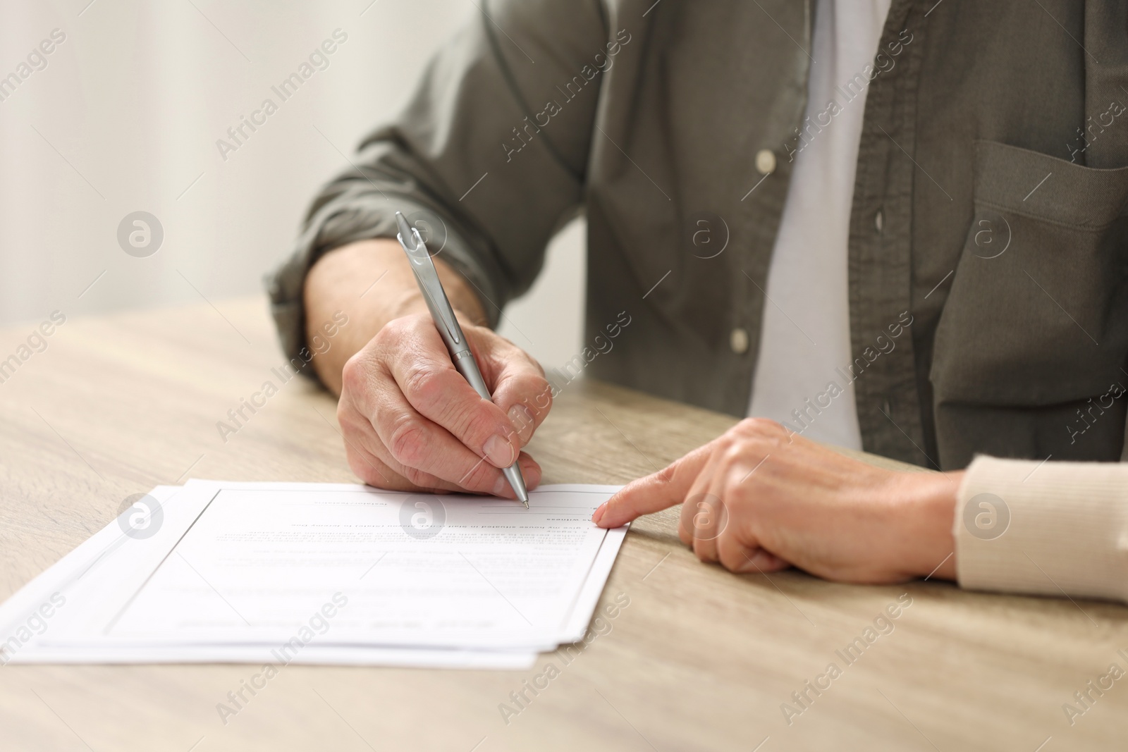 Photo of Notary pointing to senior man where to sign Last Will and Testament at wooden table indoors, closeup