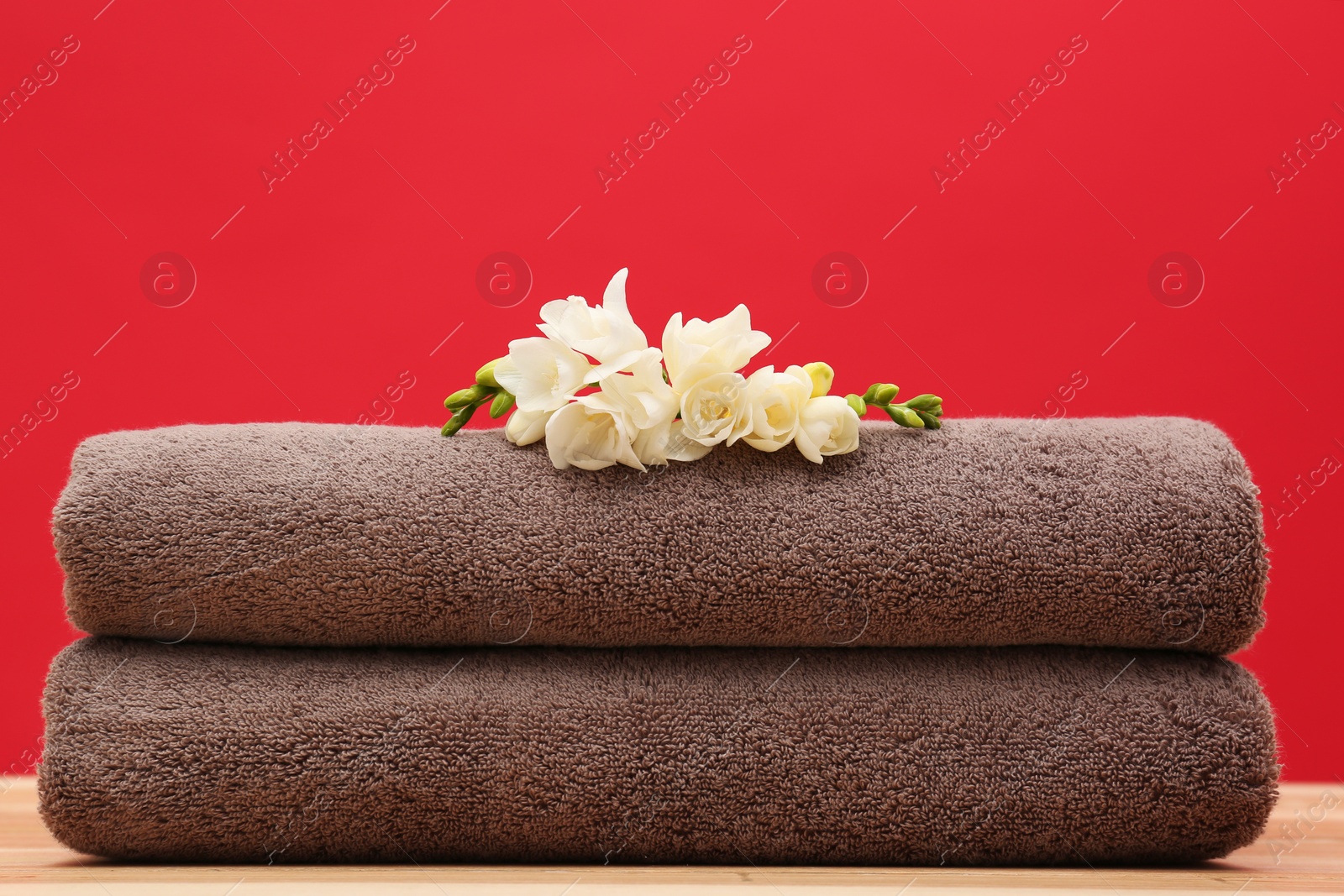 Photo of Soft clean towels with beautiful flowers on table against color background