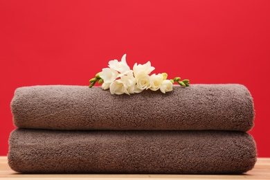 Soft clean towels with beautiful flowers on table against color background