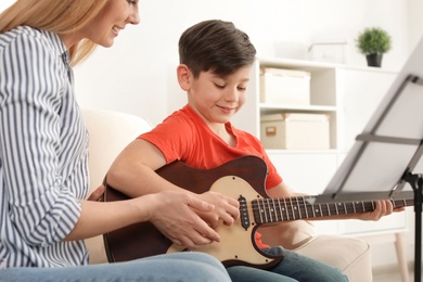 Photo of Little boy playing guitar with his teacher at music lesson. Learning notes