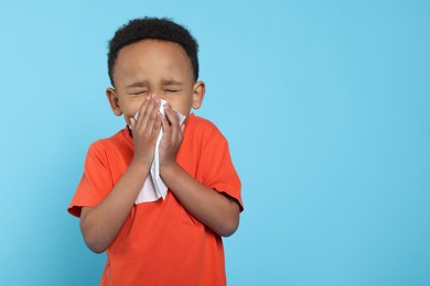 Photo of African-American boy blowing nose in tissue on turquoise background, space for text. Cold symptoms