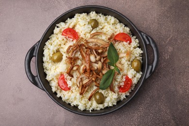 Photo of Frying pan of tasty couscous with mushrooms, olives and tomatoes on brown textured table, top view
