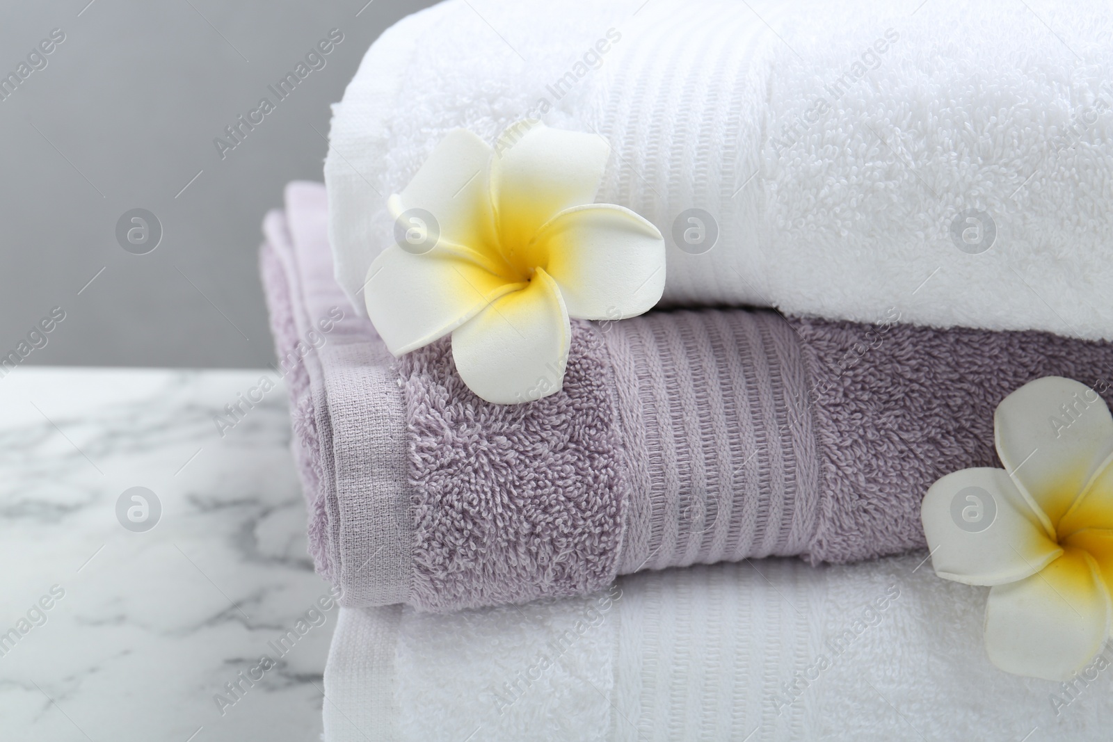 Photo of Stack of folded terry towels and plumeria flowers on white marble table, closeup