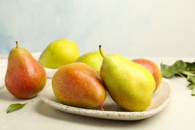 Photo of Plate with ripe juicy pears on stone table against light background