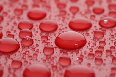 Photo of Water drops on red background, closeup view