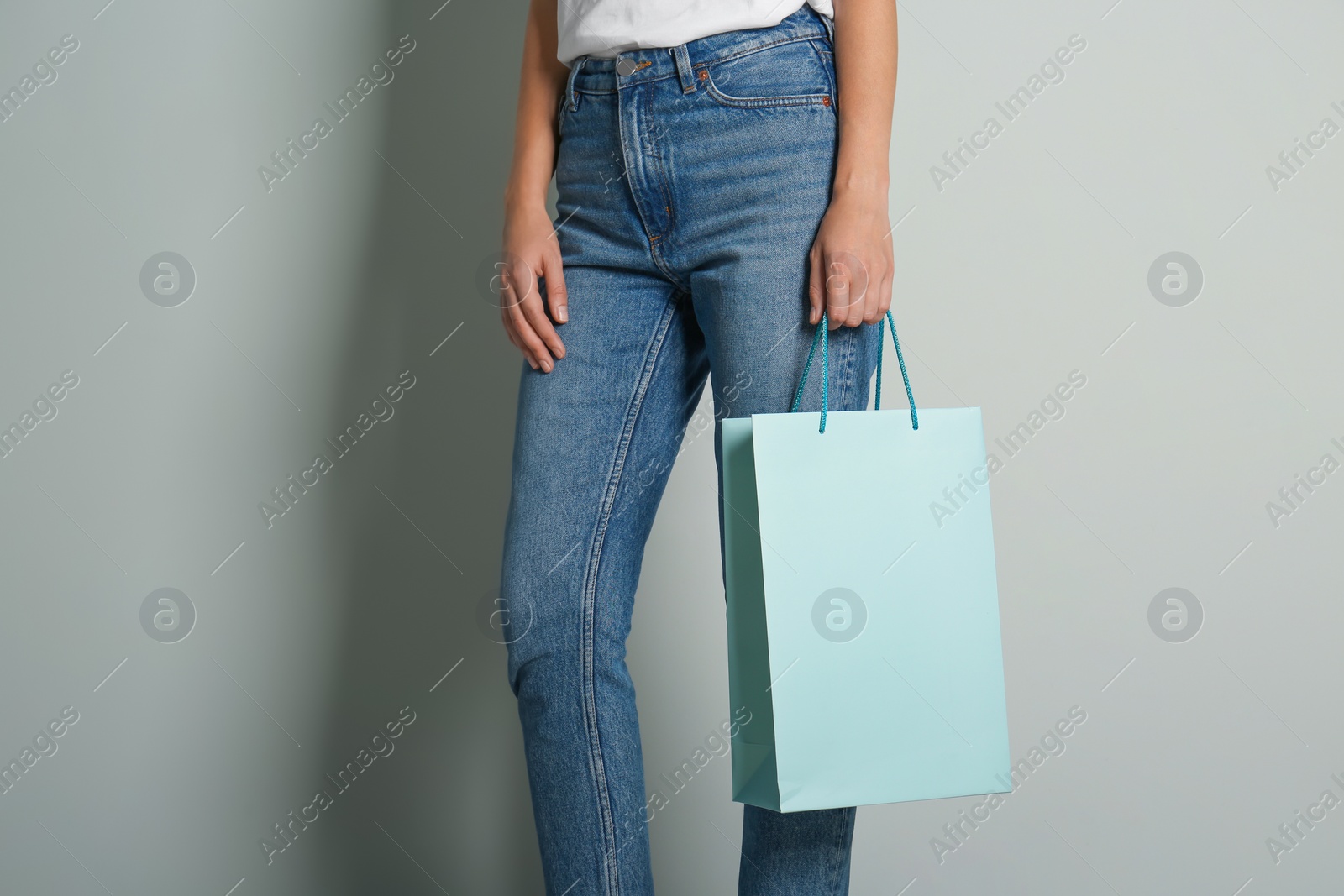 Photo of Woman with paper shopping bag on light grey background, closeup