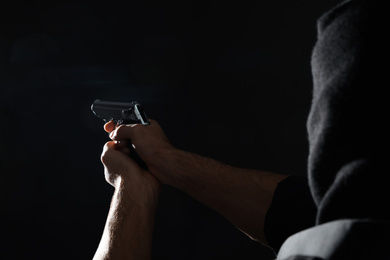 Photo of Professional killer with gun on black background, closeup