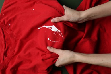 Photo of Woman holding red shirt with white paint stain on green background, top view