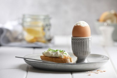 Fresh soft boiled egg in cup and sandwich on white wooden table. Space for text