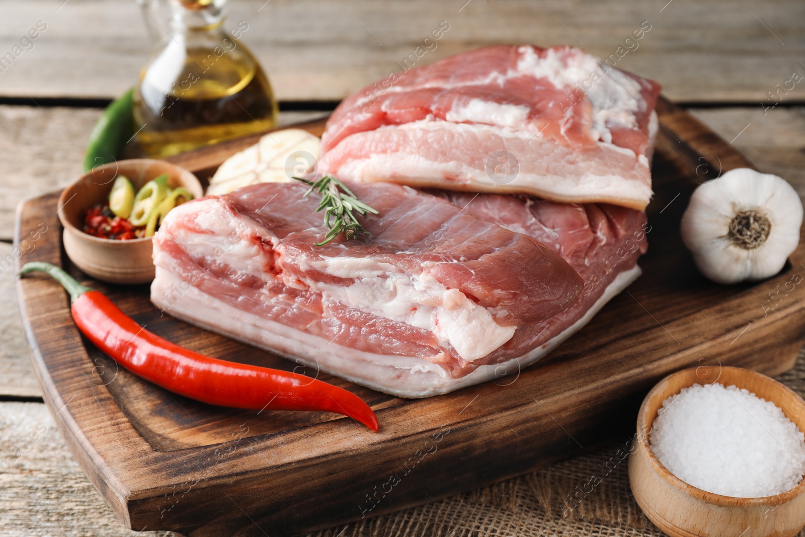 Photo of Pieces of raw pork belly, chili pepper, oil, garlic and rosemary on wooden table