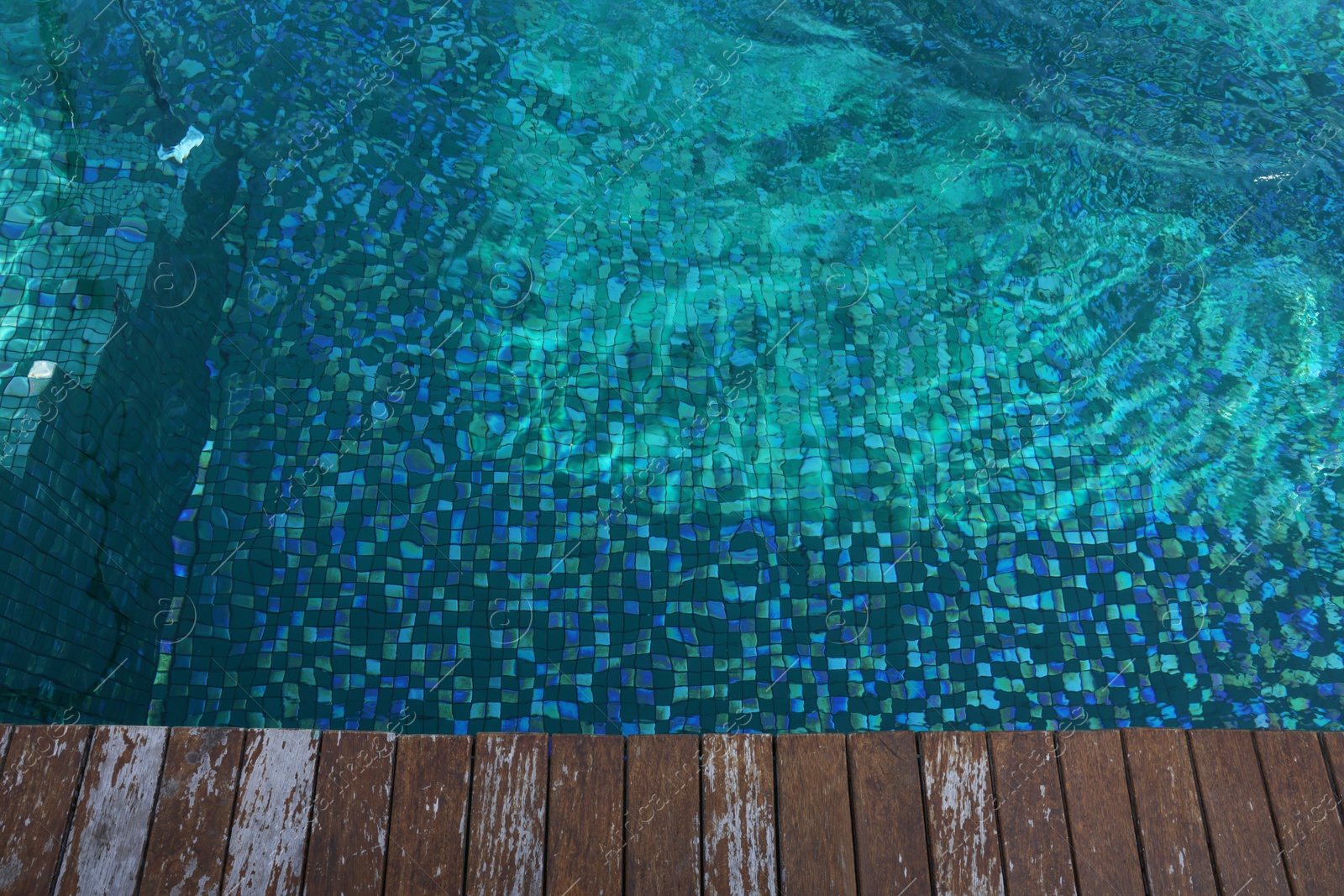 Photo of Clear rippled water in swimming pool and wooden deck outdoors, above view. Space for text