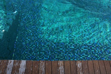 Clear rippled water in swimming pool and wooden deck outdoors, above view. Space for text