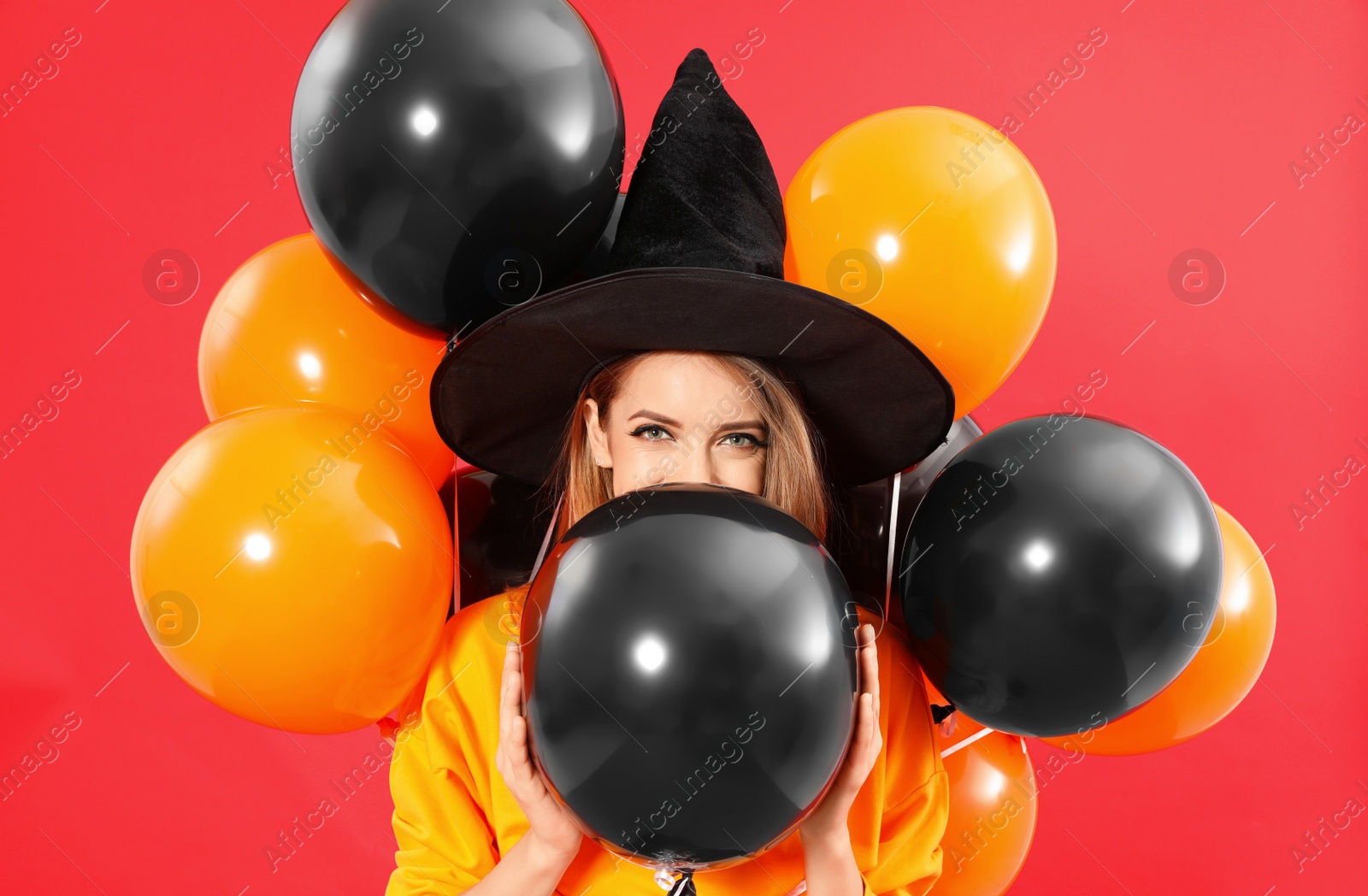 Photo of Beautiful woman wearing witch costume with balloons for Halloween party on red background