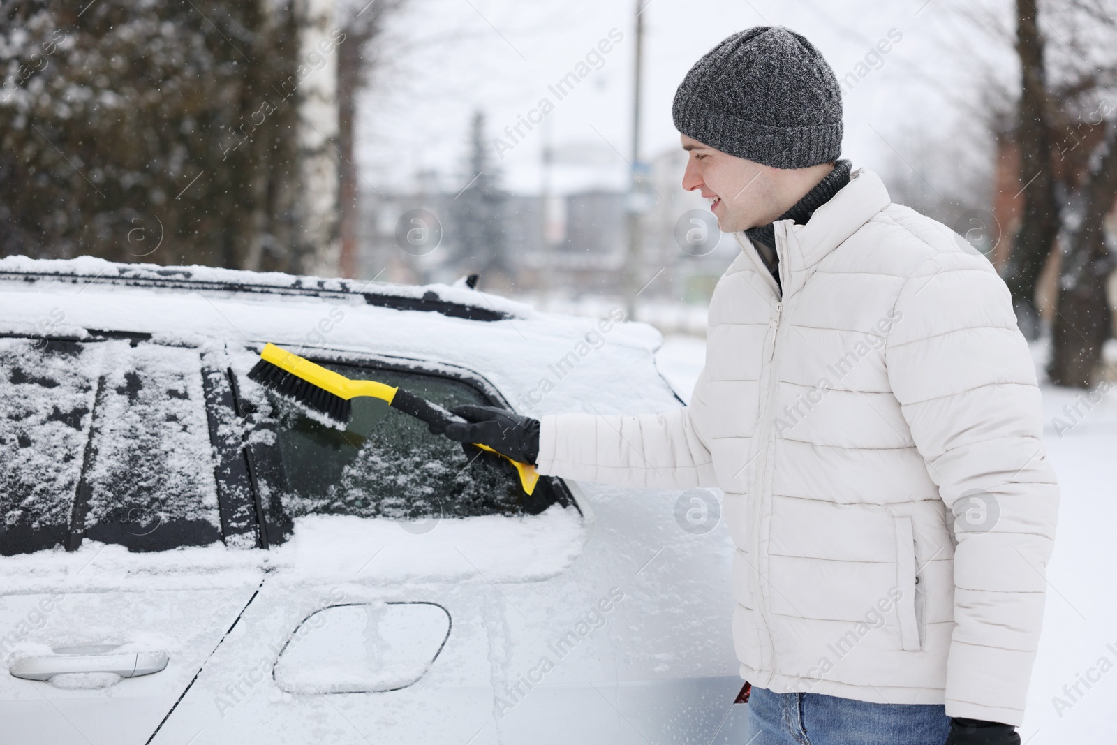 Photo of Man cleaning snow from car with brush outdoors