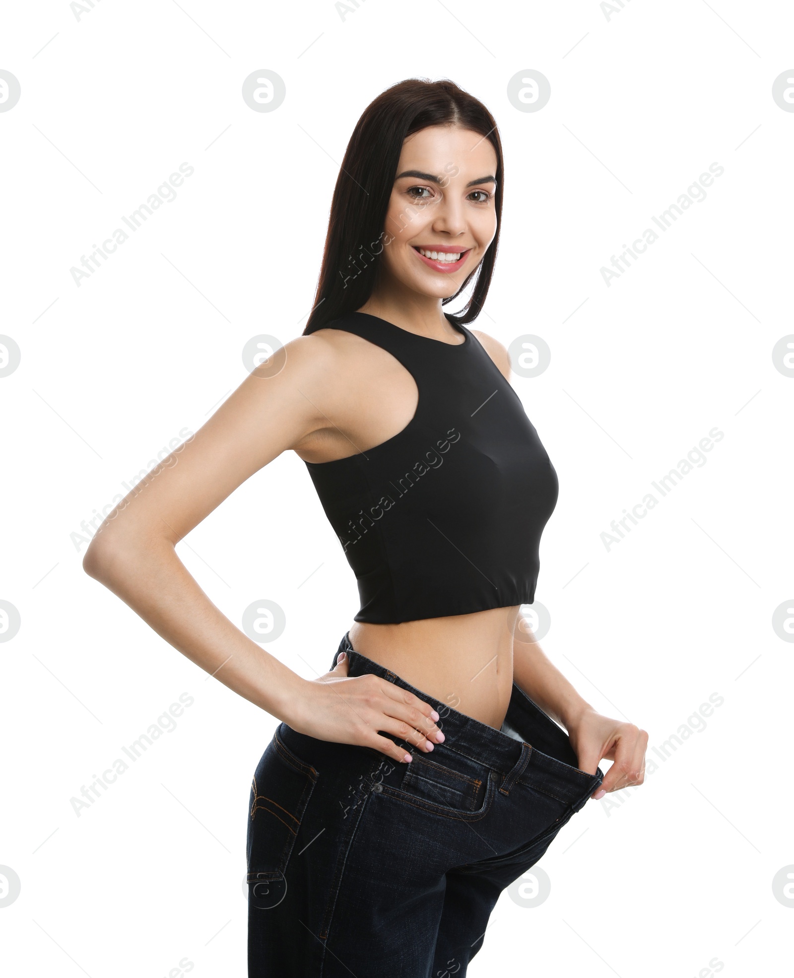 Photo of Happy young woman wearing big jeans after weight loss on white background