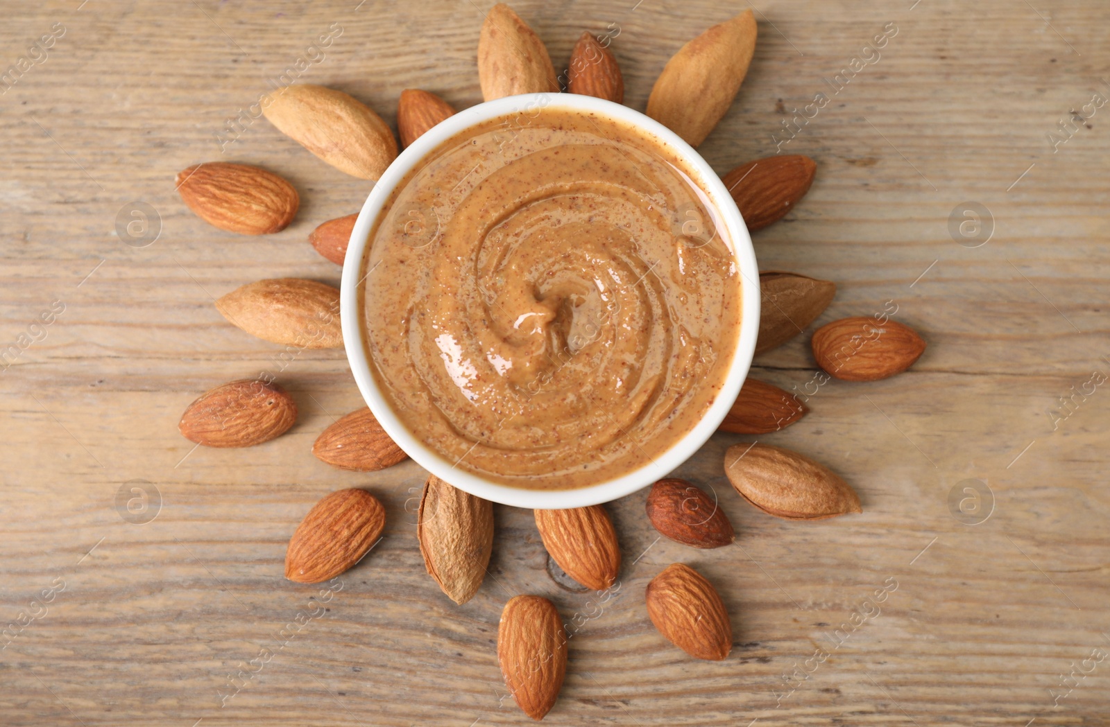 Photo of Delicious nut butter in bowl and almonds on wooden table, top view